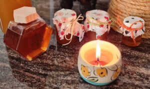 Candle in a decorated ceramic container with various honey jars in the background